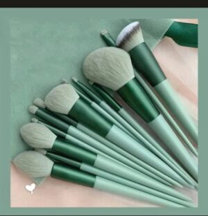 13-piece forest green makeup brush set with light gray bristles fanned out on a green velvet travel pouch.