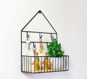 House-shaped black metal wire wall shelf with 6 hooks holding keys and a wooden basket containing a small plant and gold decor.