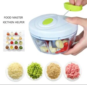 A white and green manual pull-string vegetable chopper shown with fresh vegetables and chopped chili peppers.