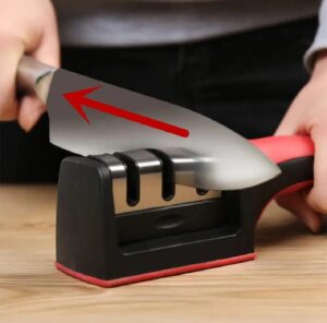 Person using a red and black 3-stage manual knife sharpener to sharpen a stainless steel chef knife.