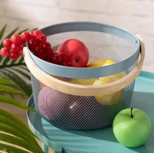 Round light blue metal mesh fruit basket with a natural wooden handle containing red grapes and apples.